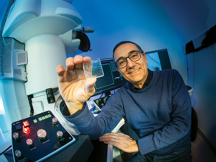 Professor Massimo Bertino sits in front of lab equipment holding up a microscope slide
