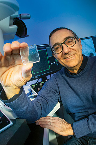 Professor Massimo Bertino sits in front of lab equipment holding up a microscope slide