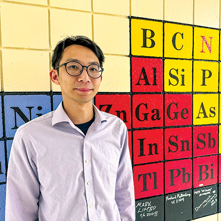 Ka Un Lao stands in front of a mural of the periodic table of elements