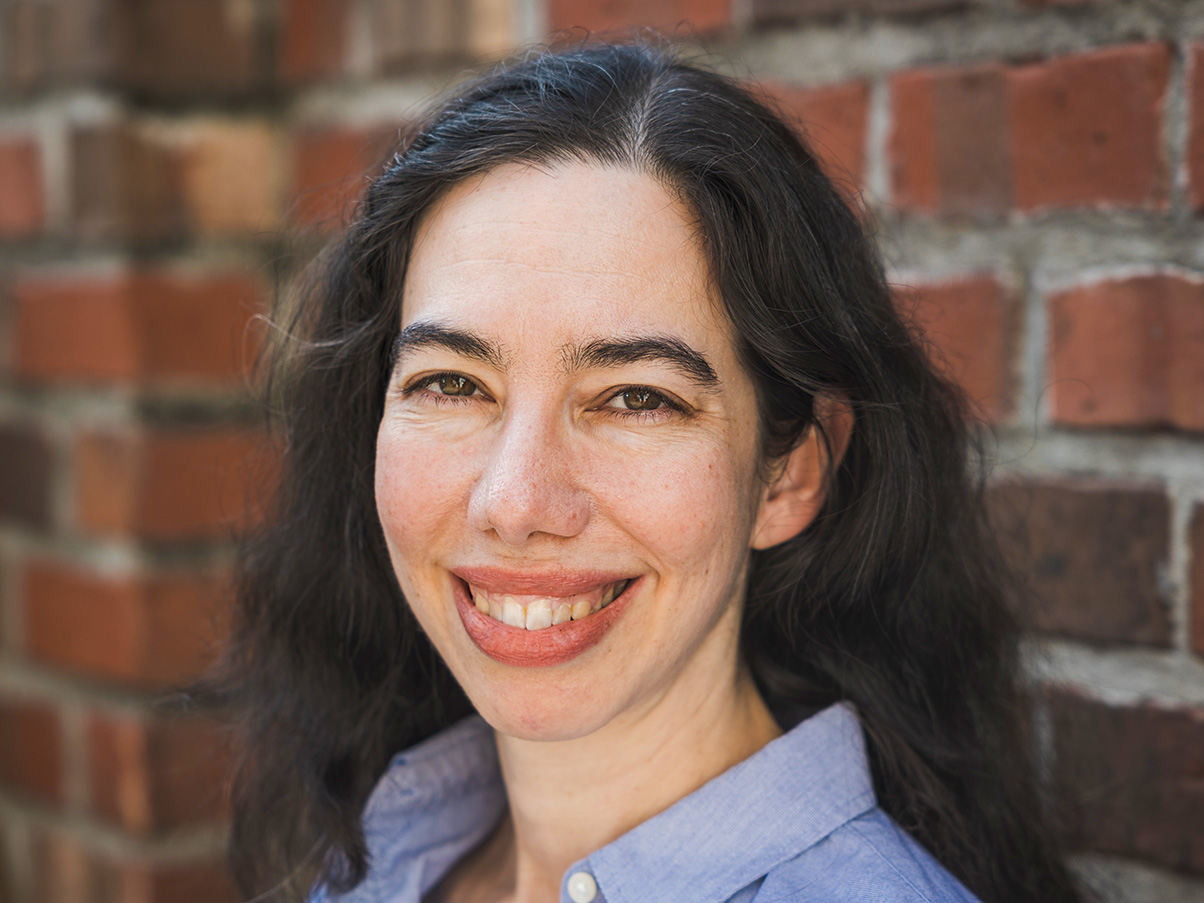 Mimi Winick stands against a brick backdrop