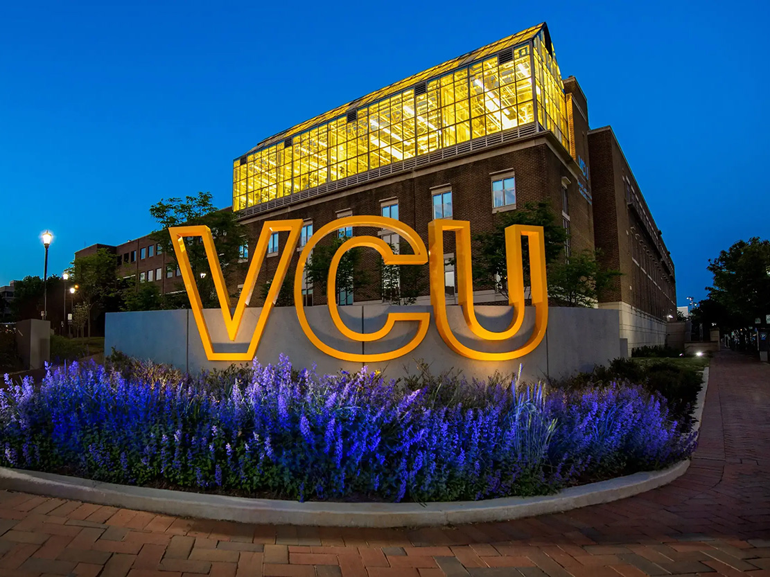 A sign that says VCU in large letters in front of the Trani Building at dusk