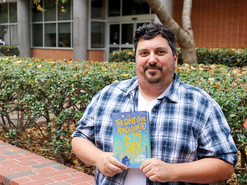 Josh Galarza stands in front of VCU's Hibbs Hall holding a copy of his book, 